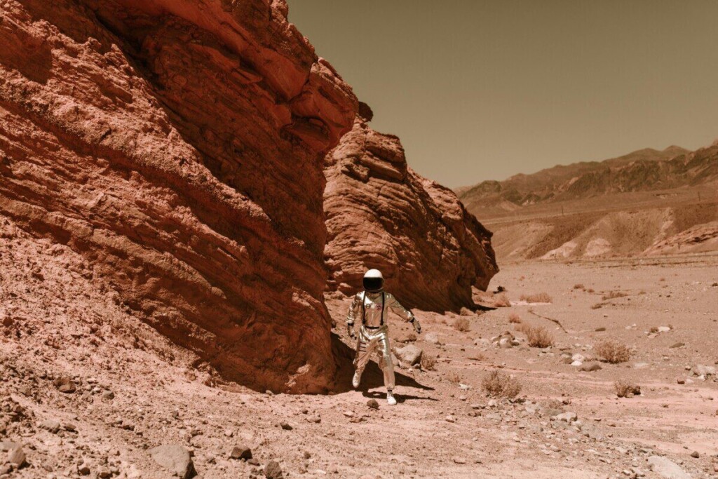 An astronaut in a spacesuit explores a barren, eroded desert, resembling Martian terrain.