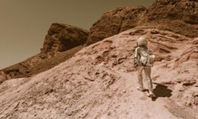 Astronaut in a space suit walking uphill on a rocky, desert-like alien planet.