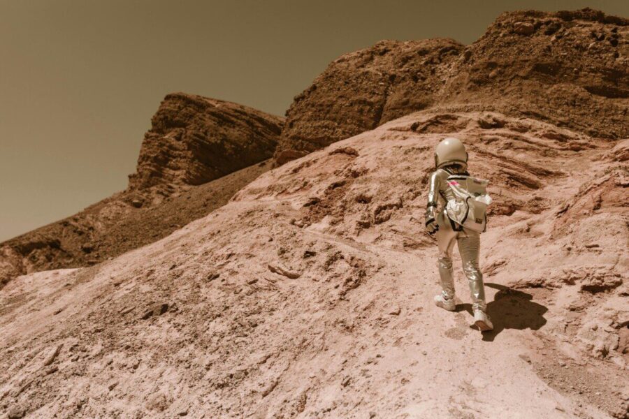 Astronaut in a space suit walking uphill on a rocky, desert-like alien planet.