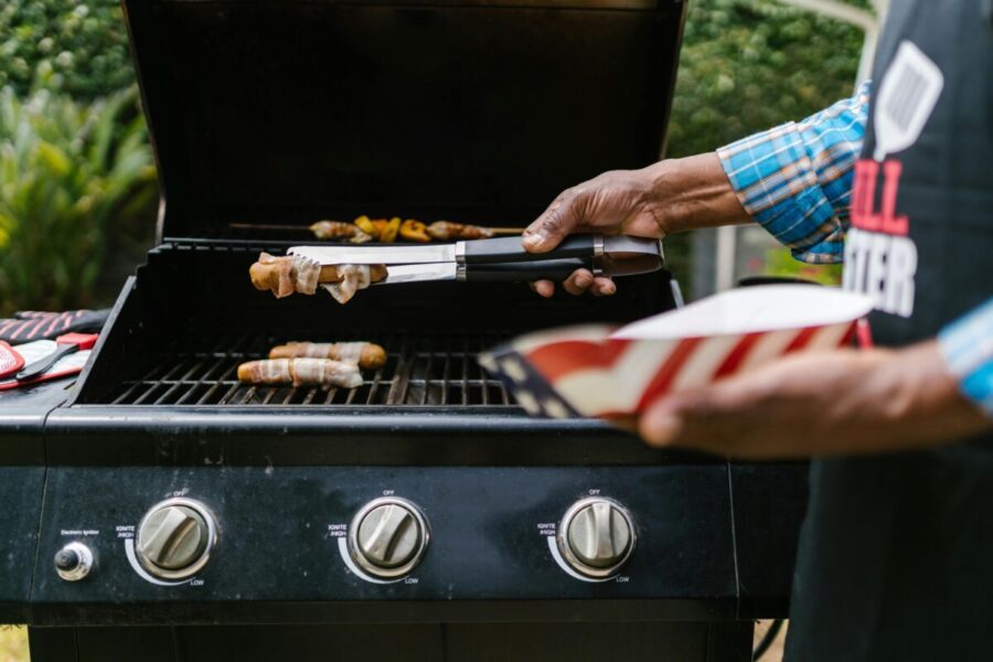 Person grilling hotdogs wrapped in bacon outdoors. Perfect for summer barbecue and celebration themes.