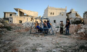 Syrian children play on a swing amidst the decaying ruins of Idlib after conflict.