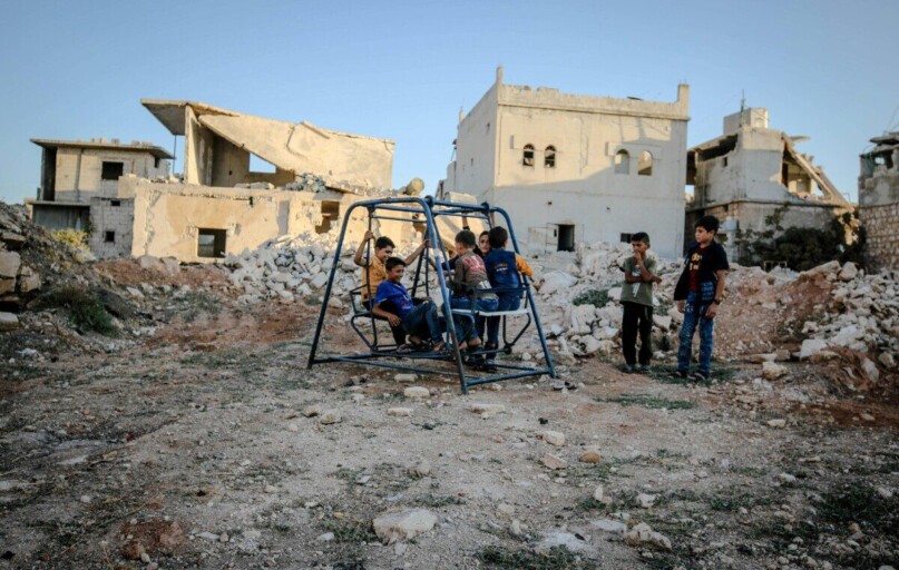 Syrian children play on a swing amidst the decaying ruins of Idlib after conflict.