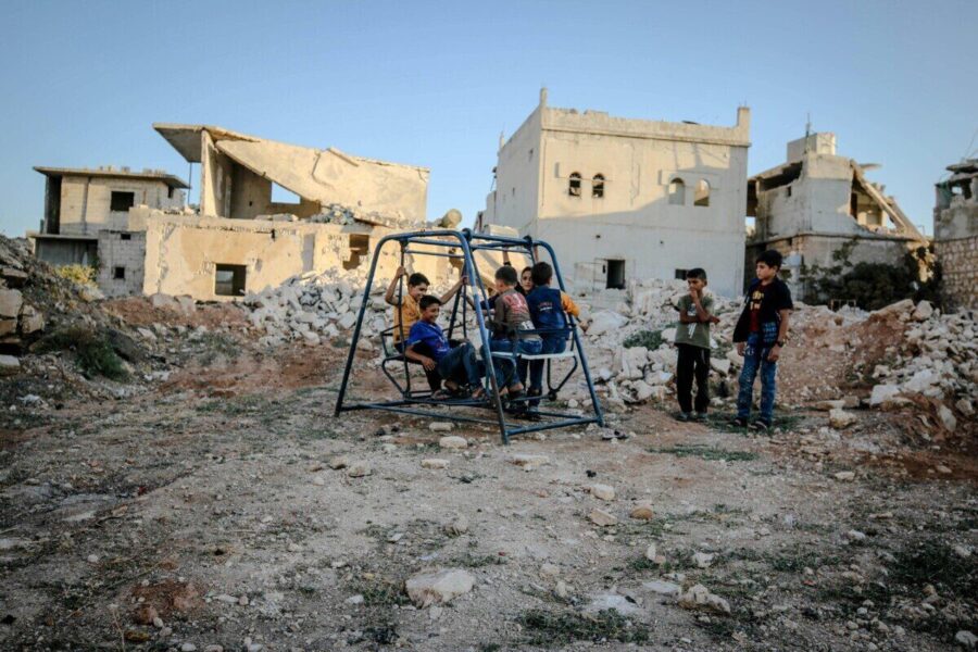 Syrian children play on a swing amidst the decaying ruins of Idlib after conflict.