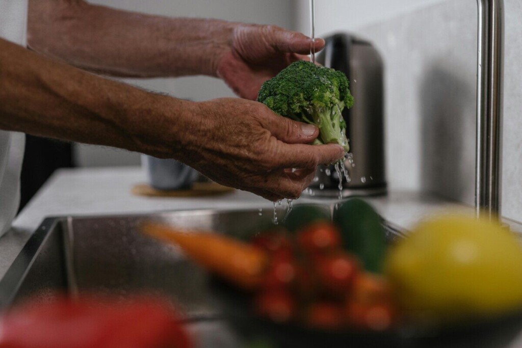 Hands washing broccoli under running water in a kitchen sink, healthy cooking concept.