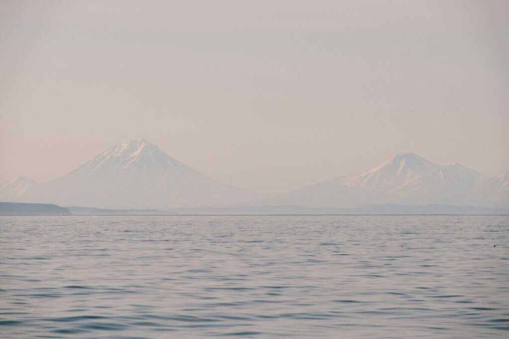 Calm ocean view with misty snowy mountains in the background under a soft pastel sky.