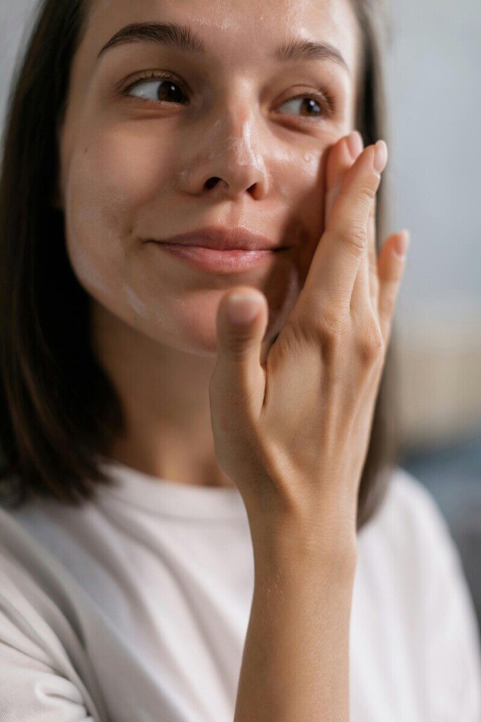 Young woman applying facial cream as part of her skincare routine, showcasing healthy and glowing skin.