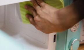 Close-up of hand cleaning a microwave with a cloth, focusing on household chores.