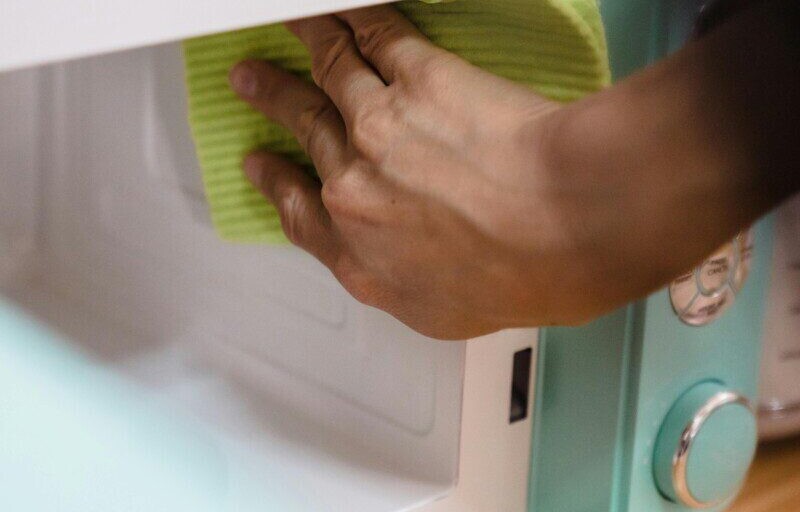 Close-up of hand cleaning a microwave with a cloth, focusing on household chores.