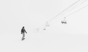 Snowboarder gliding under ski lifts in snowy Breckenridge, Colorado.