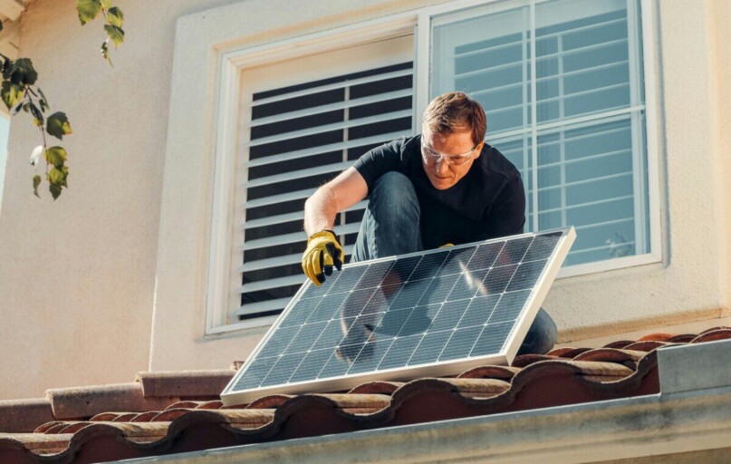Solar technician installing a photovoltaic panel on a rooftop, promoting renewable energy.