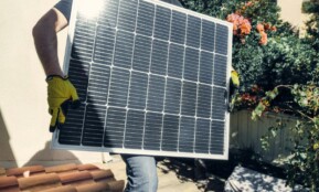 Technician carrying solar panel on rooftop. Clean energy installation outdoors.
