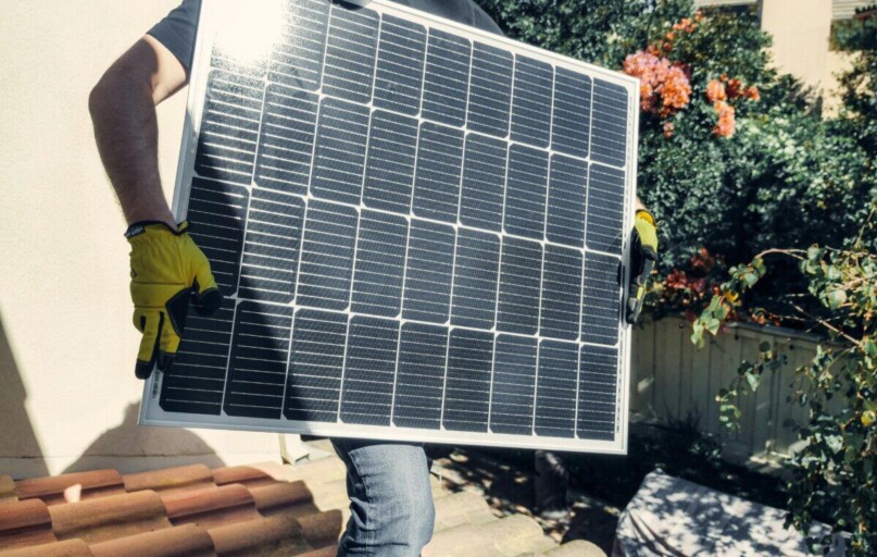 Technician carrying solar panel on rooftop. Clean energy installation outdoors.