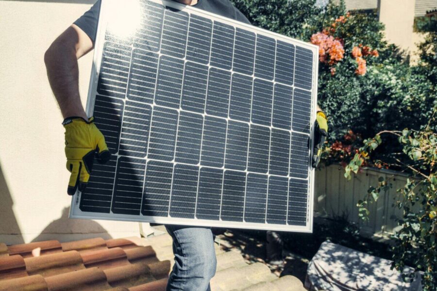 Technician carrying solar panel on rooftop. Clean energy installation outdoors.