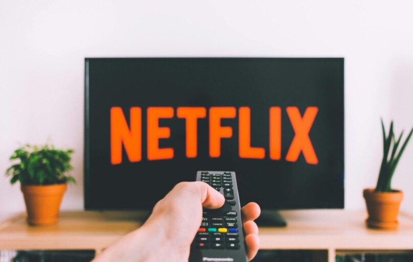 A hand holding a TV remote in front of a screen with Netflix, perfect for streaming and movie night themes.