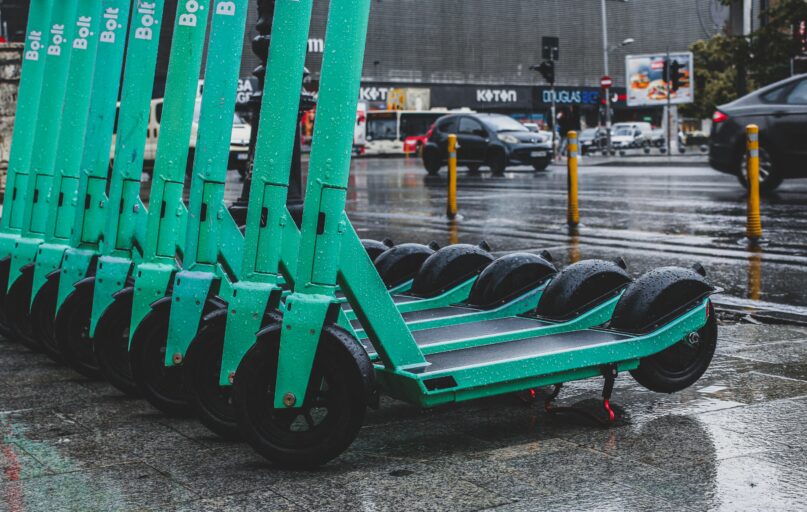Rain-soaked electric scooters lined up on a city street, reflecting urban transportation.