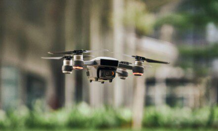 Close-up of a modern quadcopter drone hovering outdoors with blurred greenery background.