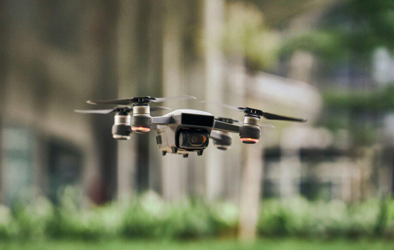 Close-up of a modern quadcopter drone hovering outdoors with blurred greenery background.