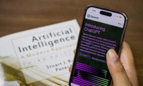 Close-up of a smartphone displaying ChatGPT app held over AI textbook.