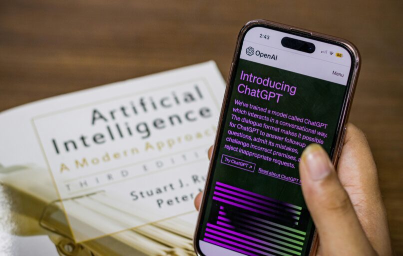 Close-up of a smartphone displaying ChatGPT app held over AI textbook.