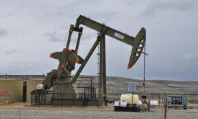Oil pump jack and equipment at remote industrial site under cloudy sky.