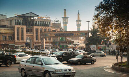 Bustling Tehran street scene with cars, mosque minarets, and traditional architecture.