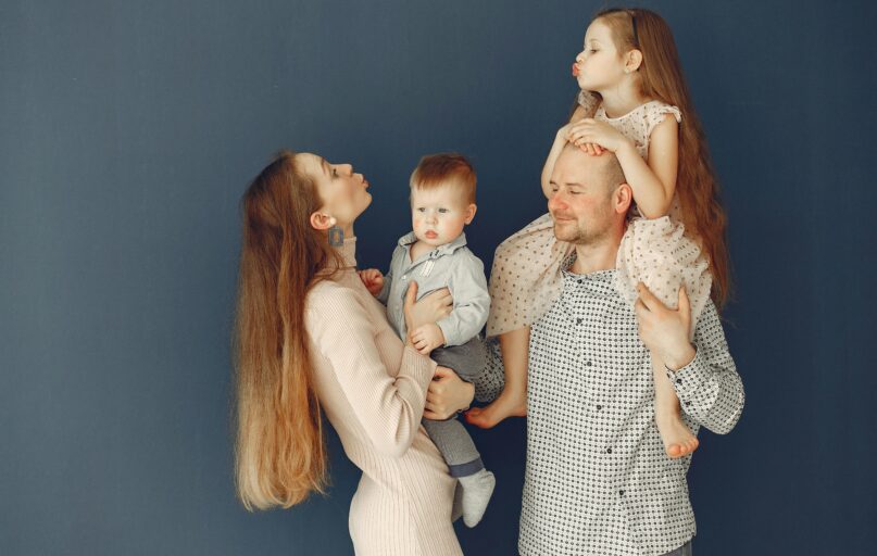 Portrait of a joyful family with parents and kids showing love and affection against a blue background.