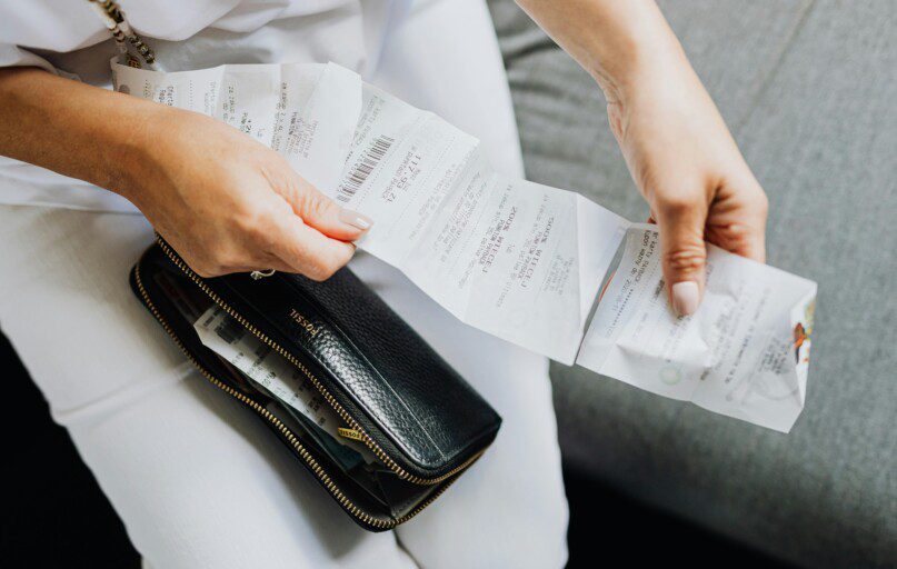 Close-up of a woman's hands managing multiple receipts taken from a black wallet.