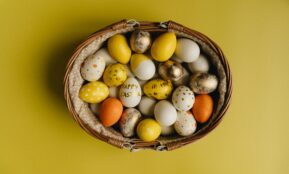Basket of painted Easter eggs on yellow background. A festive springtime display.