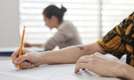 Close-up of student's hands writing on exam sheet, indoors with blurred background.