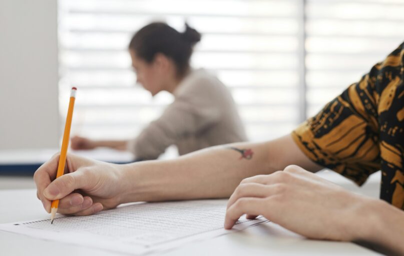 Close-up of student's hands writing on exam sheet, indoors with blurred background.