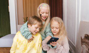 Three children indoors sharing a fun moment with a smartphone, displaying joy and togetherness.