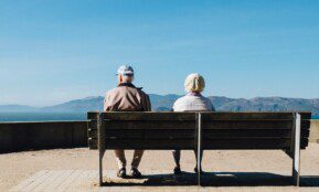 man and woman sitting on bench facing sea