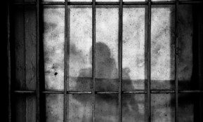 a shadow of a person behind bars in a jail cell