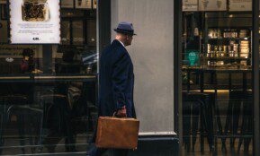 man in black suit jacket and blue hat standing in front of store