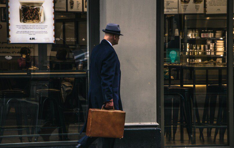 man in black suit jacket and blue hat standing in front of store