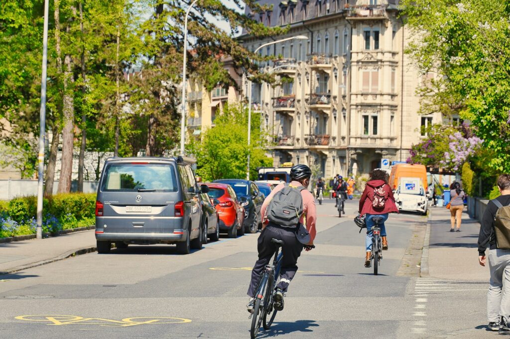Cyclists ride down a tree-lined street in a city.