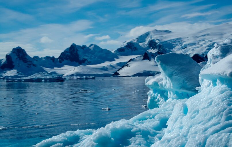 a large iceberg floating on top of a lake surrounded by snow covered mountains