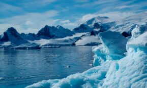a large iceberg floating on top of a lake surrounded by snow covered mountains
