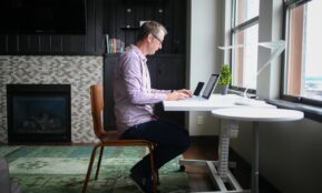man in gray dress shirt sitting on brown wooden chair using macbook pro