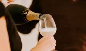 person holding black labeled bottle pouring on clear glass