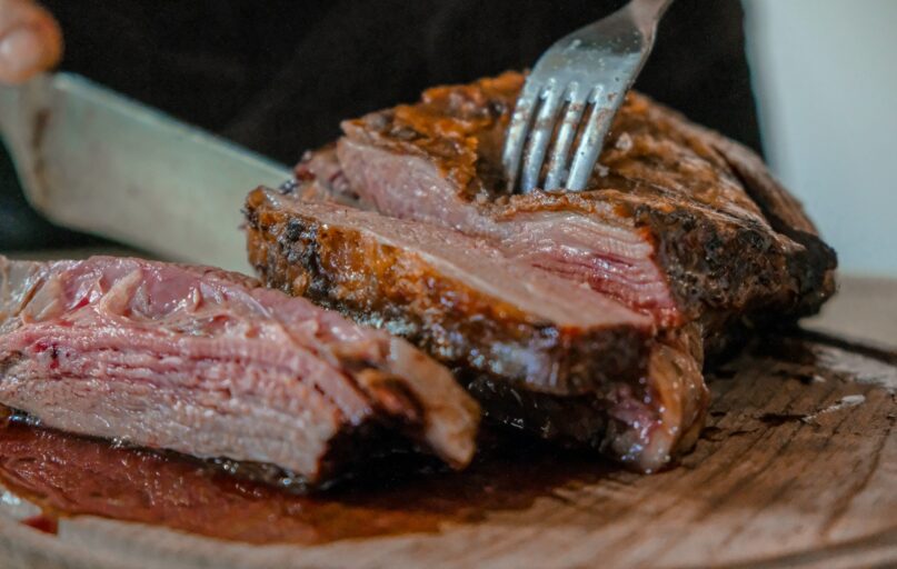 person slicing a meat on brown wooden board