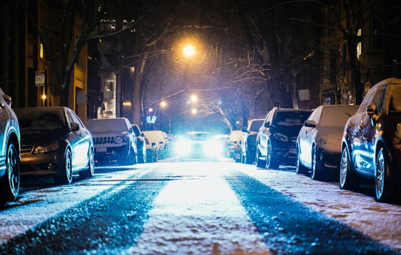 cars parked on both sides of the street during snowy nighttime