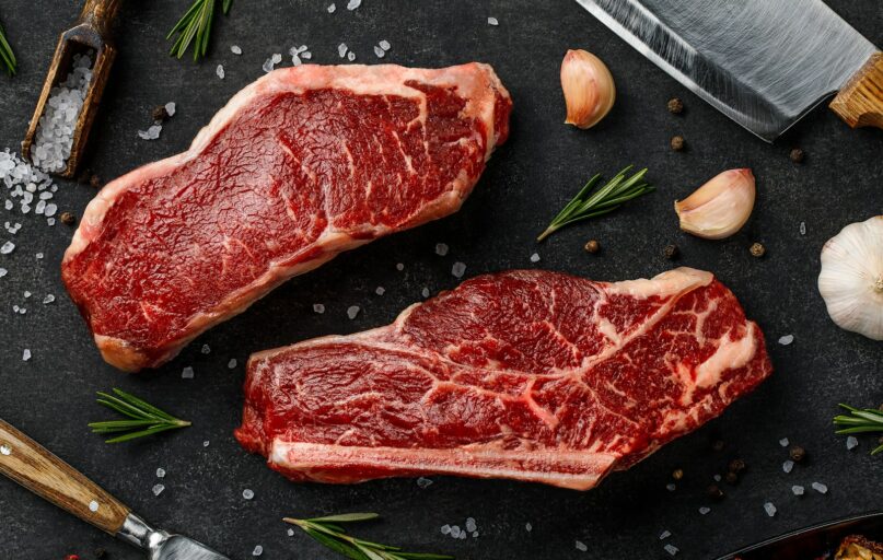 two steaks on a cutting board next to garlic, garlic, and a knife