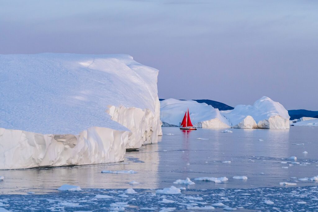 a red sailboat in the water near icebergs