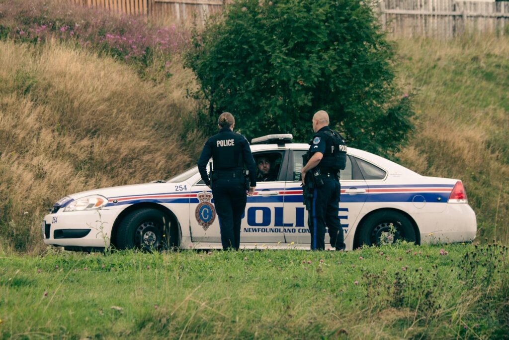 2 men standing beside white and blue police car