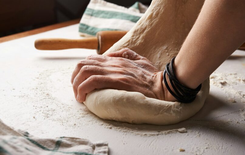 person making dough beside brown wooden rolling pin