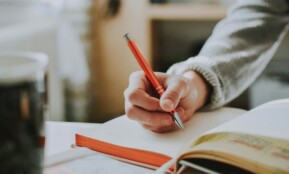 person holding on red pen while writing on book