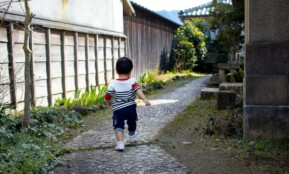 boy in black and white stripe t-shirt and black shorts standing on gray concrete pathway