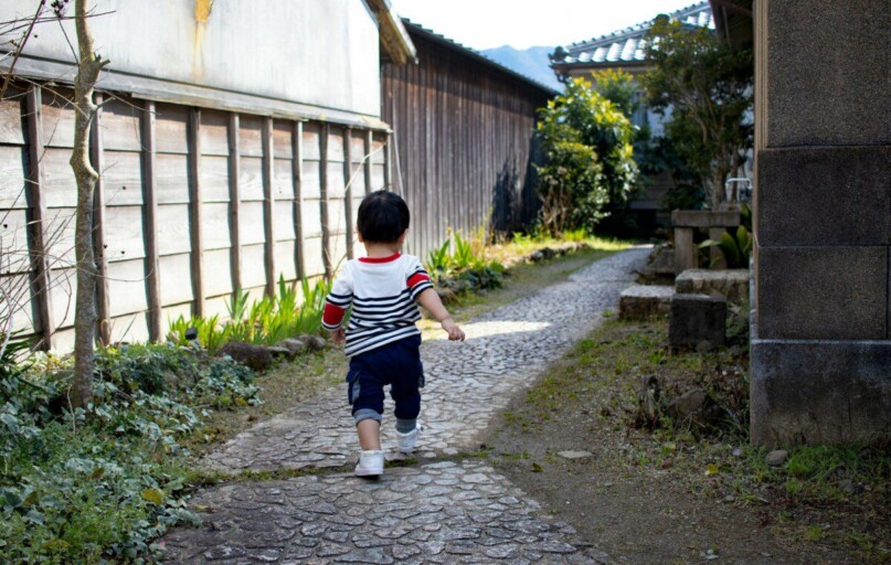 boy in black and white stripe t-shirt and black shorts standing on gray concrete pathway