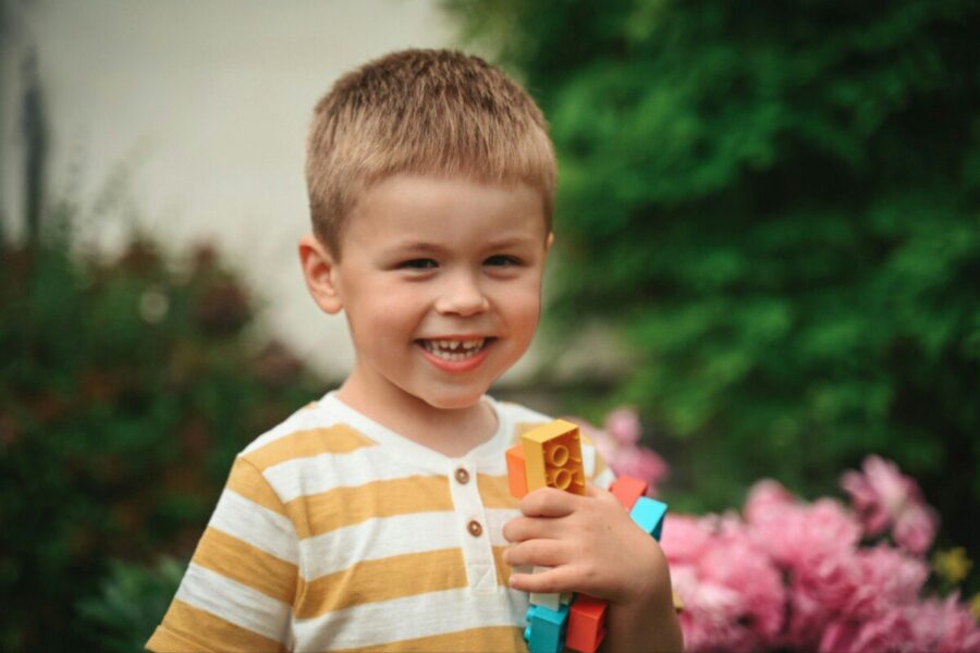 Young boy smiling, holding colorful building blocks outdoors.